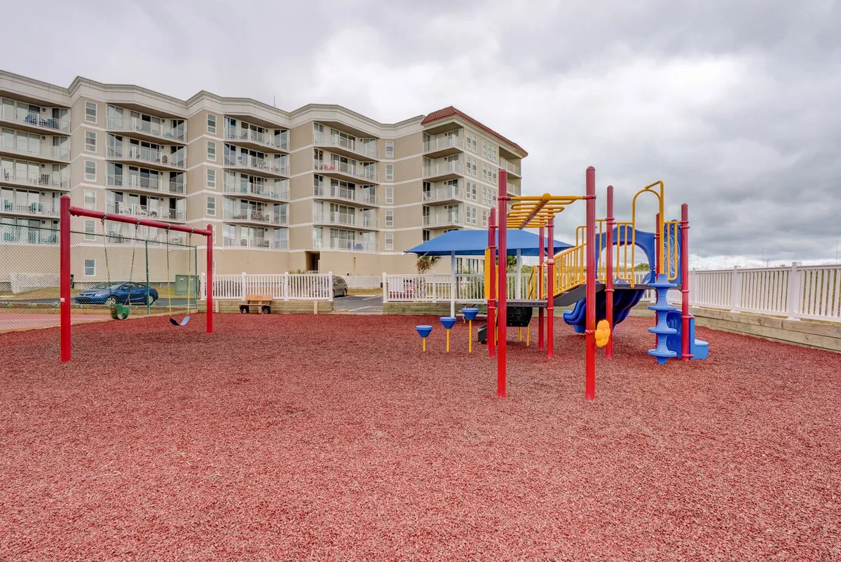 A joyful scene focused on the colorful playground equipment with swings and a spacious play area, where children are actively playing and families are gathered nearby. The atmosphere is energetic and welcoming for kids of all ages.