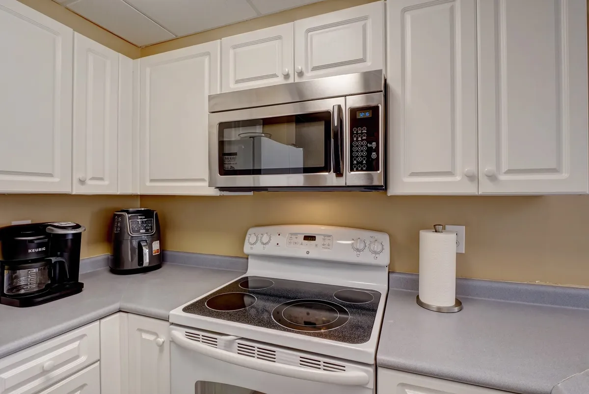 A detailed kitchen view featuring a stove, microwave, coffee maker, and prominently, an air fryer. The setup is inviting and practical, showcasing the modern appliances and countertop space perfect for preparing meals or beach picnics.