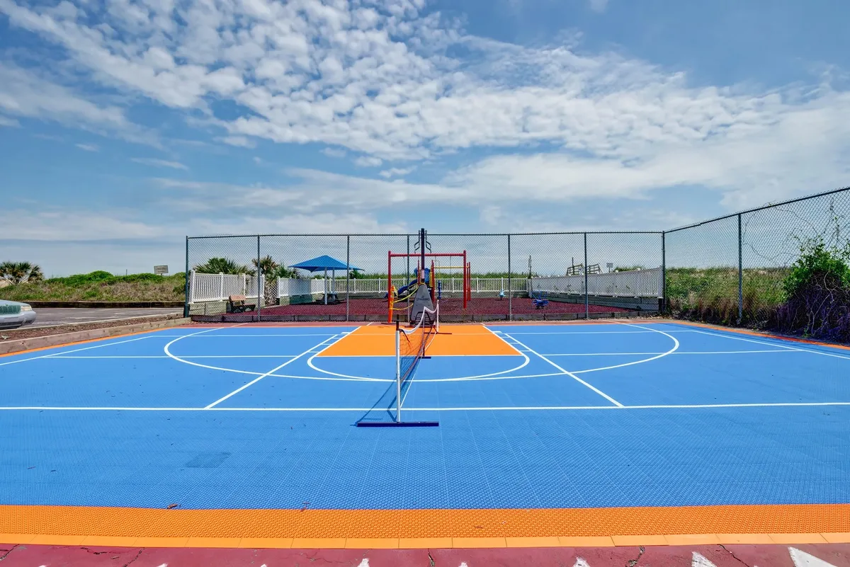 An exterior shot featuring a colorful multi-use basketball and tennis court, adjacent playground equipment, and lush greenery. The diverse recreational spaces offer visual cues for friendly competitions and active fun for all ages.