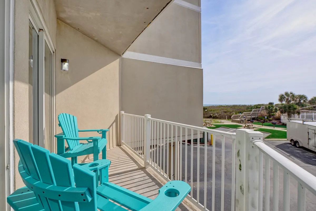 A private balcony with turquoise Adirondack chairs overlooks a tranquil landscape. The balcony railing hints at elevated views, while the open, airy setting invites moments of peaceful reflection or evening relaxation.