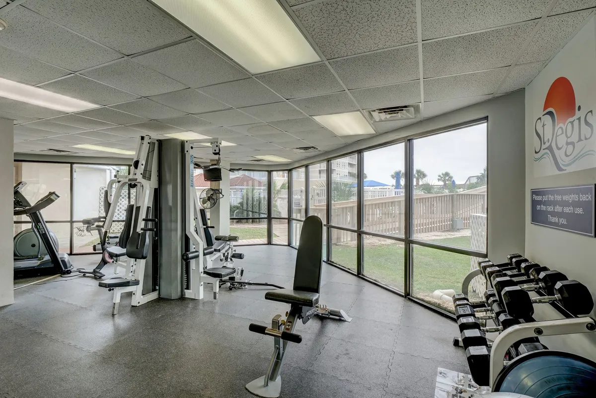 The fitness center boasts modern exercise equipment, large windows letting in natural light, and the St. Regis logo, fostering an atmosphere of lively, health-focused activity.
